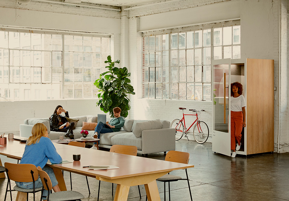 A modern, open-plan office with people collaborating on a sofa and at a large table.