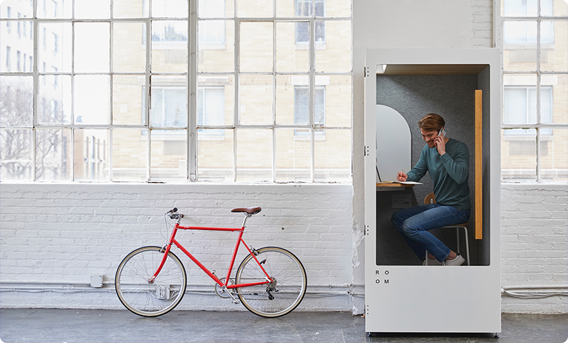 A man working in a modern office phone booth next to a red bicycle.